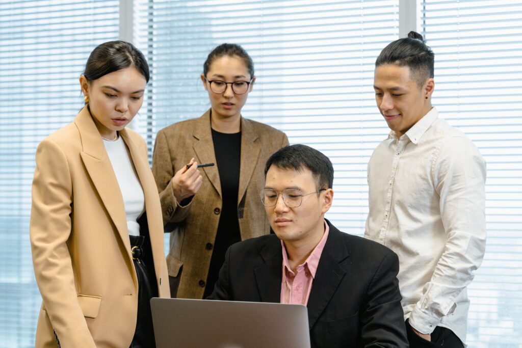 Group of professionals gathered around a laptop for a work meeting in a modern office.